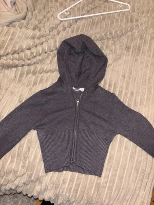 Mörkgrå cropped hoodie med dragkedja - Säljer en mörkgrå cropped hoodie med dragkedja framtill. Hoodien är stickad och har långa ärmar samt ribbad nederkant och muddar. Perfekt för dig som gillar en enkel men snygg stil med lite edge. snygg passa xs-xxs