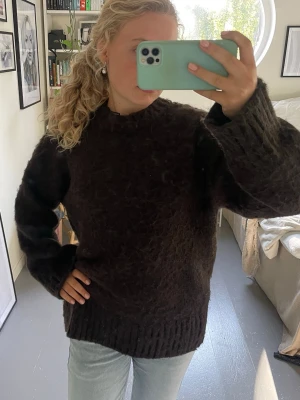 Mörkbrun fluffig stickad tröja Monki - Mysig mörkbrun stickad tröja från Monki med oversized passform och fluffig textur. Tröjan har rund halsringning, långa ärmar och breda ribbade muddar vid ärmslut och nederkant. Perfekt för kalla dagar och enkel att styla med jeans eller kjol.