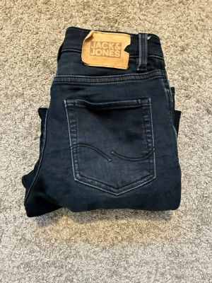Mörkblå slitna jeans Jack & Jones - Snygga mörkblå jeans från Jack & Jones med slitningar på låren och knäna. Klassisk femficksmodell med läderpatch bak i midjan. Jeansen har smal passform och är tillverkade i ett mjukt denimtyg som ger en bekväm känsla.