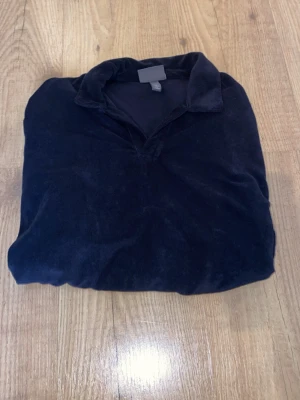 Mörkblå velourtröja från H&M - Mjuk och skön mörkblå velourtröja från H&M med klassisk krage och relaxed fit. Perfekt för dig som gillar en avslappnad stil. Tröjan har en enkel design utan tryck eller mönster och är tillverkad i ett lent velourmaterial.