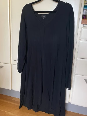 Svart långärmad klänning från Zizzi - En svart långärmad klänning från Zizzi med v-ringning. Klänningen har en enkel och stilren design med lös passform och är tillverkad i ett mjukt material som känns skönt mot huden. Perfekt för dig som gillar minimalistisk stil.