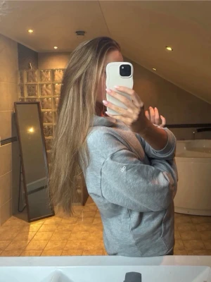 Ljusgrå hoodie med huva - Säljer en stilren ljusgrå hoodie med huva och långa ärmar. Hoodien har en avslappnad passform och är tillverkad i mjukt material, perfekt för en chill och bekväm look. Diskret logga på ärmen ger en clean vibe.