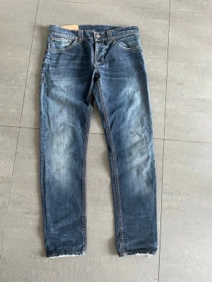 Dondup jeans - Säljer ett par blå jeans med rak passform. Jeansen har fem fickor, klassisk knappgylf och rå, fransig kant vid bensluten. Materialet är denim i bomull och färgen är mellanblå med ljusare partier.