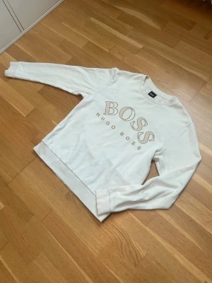 Hugo boss tröja  - Tjena, säljer min vita Hugo Boss sweatshirt med stort guldfärgat BOSS-tryck och texten HUGO BOSS på bröstet. Tröjan är relativt sällsynt och inte något man ser varje dag. Perfekt för en clean och stilren look.