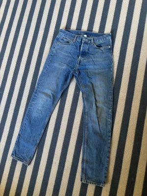 Weekday blå jeans 28/30 Pine - Klassiska blå jeans med rak passform och hög midja. Jeansen har fem fickor, knappgylf och subtila slitningar på låren för en avslappnad look. Perfekta till sneakers eller boots och passar till många olika stilar.