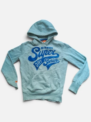 Ljusblå hoodie från Superdry - Snygg ljusblå hoodie från Superdry med stor blå logga och text på bröstet. Hoodien har huva, känguruficka och ribbade muddar vid ärmar och nederkant. Perfekt för en avslappnad och cool stil.