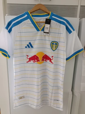 Leeds United Matchtröja – Muharemović - Säljer en helt ny och oanvänd Leeds United fotbollströja från Adidas med alla originallappar kvar. Tröjan har tryck på ryggen med MUHAREMOVIĆ #5.