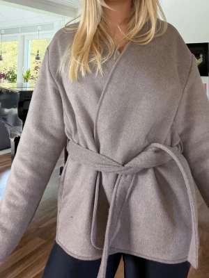Beige omlottkappa med knytskärp - Snygg beige kappa med omlottmodell och knytskärp i midjan. Perfekt för lager på lager! Nästan aldrig använd och köpt i våras🥰
