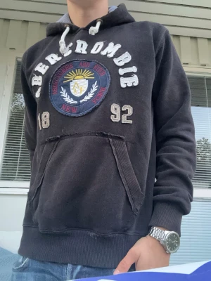 Svart Abercrombie & Fitch Vintage Hoodie - En supersnygg svart hoodie från Abercrombie and Fitch vintage-stil🤩Tröjan har ett tryck från Abercrombie med både text i tyg och dess logotyp👌Tröjan är dessutom i mycket gott skick utan några defekter👍Längd 68 cm. Bredd mellan armhålor 58cm.