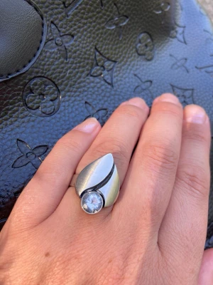 Modern silverring med stor bergkristall - Säljer en snygg och unik silverring med modern, böljande form och en stor, klar bergsten framtill. Ringen har en cool, stilren design som verkligen sticker ut och passar perfekt för dig som gillar statement-smycken. Den är från silver och från märke Karl Laine. Ringen är justerbar.