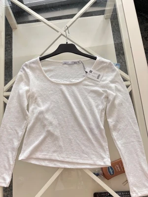 Vit ribbad långärmad topp - Säljer en enkel och stilren vit topp med ribbad struktur och lång ärm. Toppen har en rundad halsringning och är perfekt för att matcha med olika outfits. Materialet känns mjukt och stretchigt.