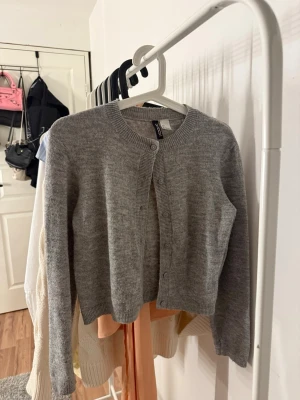 Grå kofta från Divided H&M - Säljer en enkel och stilren grå kofta från Divided H&M. Koftan har rund halsringning, knappar framtill och ribbade muddar vid ärmslut och nederkant. 