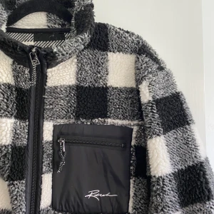 black & white checkered zipped teddy jacket  - size is men’s S but I have always worn it and I am a girl (180cm tall) so I call this unisex. checkered zipped teddy kind of jacket or bomber thing. very cozy, kind of cool, brand is called Review
