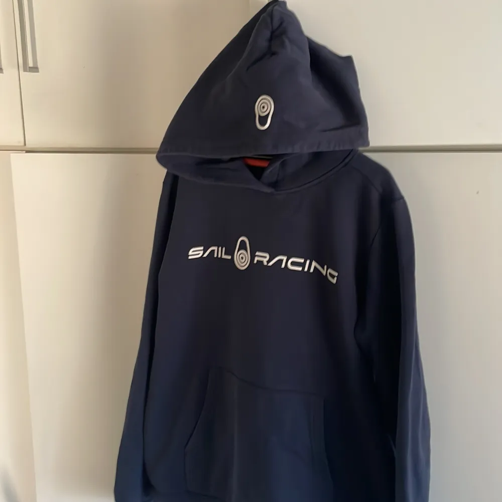 Mörkblå Sail Racing hoodie i bra skick. Tröjan har luva och magficka, som ni ser! Ge gärna prisförslag :). Hoodies.