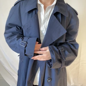 Trenchcoat  - Säljer denna snygga trenchcoaten. Den är en stor M skulle jag säga, så den sitter oversized på en M. Fint skick, mörkblå. Lite tjockare material så passar perfekt till hösten. 