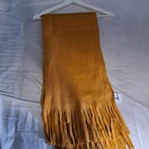 En gul oanvänd stickad halsduk från lager157. Den första bilden motsvarar mer färgen på halsduken. Ungefär 2m lång 