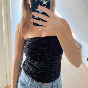 Glittrig festtopp - Säljer en glittrig svart festtopp med paljetter. Den är bandeu och kan även användas som kjol. Köpt i en gatubutik i Spanien för 25 euro! Perfekt till nyår, fester eller liknande!