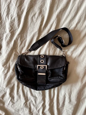 Prada väska nylon och läder - Snygg och praktisk väska från Prada i nylon och skinn mer silvriga detaljer i mycket bra skick. Kan både användas som handväska och axelremsväska då banden är justerbara.   Höjd: ca 17 cm  Bredd: ca 27 cm Djup: ca 9 cm