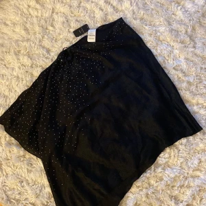 Glittrig poncho  - En svart glittrig poncho med silver stenar. Nyskick och aldrig använd. Storlek: One Size