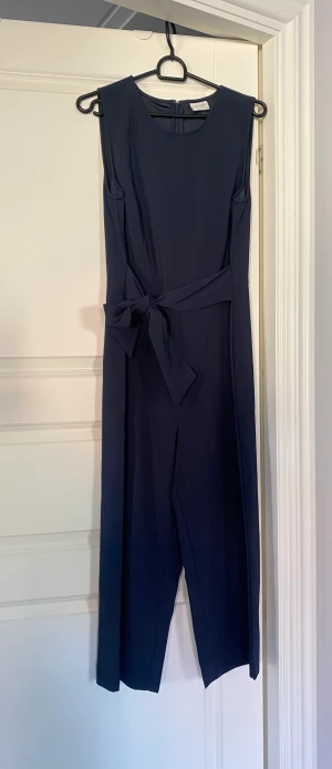 Marinblå byxdress - Snygg, marinblå byxdress med band att knyta i midjan.  Ankellånga på mig som är 162 cm. 