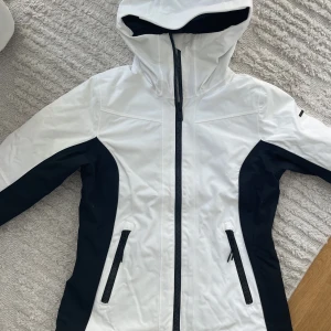 Skidjacka - Vit skidjacka med svarta detaljer! Från Everest och i väldigt fint skick. Sparsamt använd och fortfarande väldigt vit i färgen helt utan fläckar eller liknande. Tumhål i ärmarna, nypris ligger runt 1500kr. Säljer pga blivit för liten för mig⛷️
