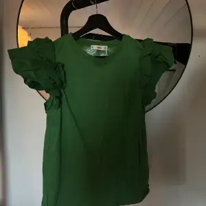 En grön tröja med volang. I storlek M men skulle säga att den är med i S. Aldrig använd 
