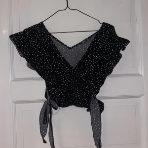 Svart topp med rosetter i midjan - Svart topp med vita prickar, smickrande passform