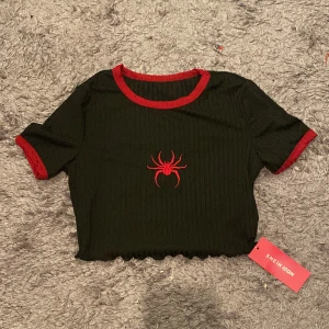  T-shirt -  svart ribbad T-shirt med röda kanter och en röd spindel på i storlek M. 