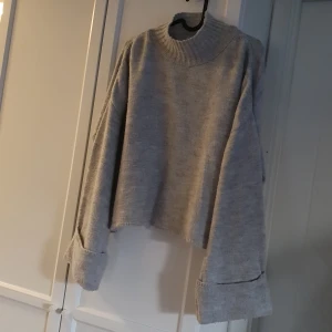 Stickad tröja  - Ljusgrå stickad tröja med lång ärm, uppvikta ärmar. 