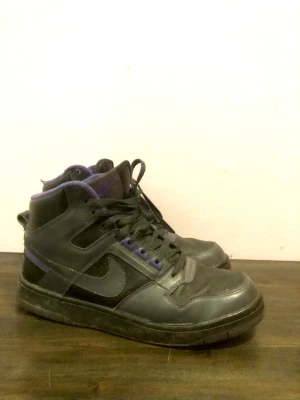 Nike sneakers 42.5 - Snygga klassiska high sneakers i svart och lila. Köpte de begagnade, sulan på vänster sko har släppt lite men det stör inte alls när man går i dom, det kan lagas om dom limmas skulle jag tro. I övrigt i fint använt skick! Stl 42.5 men mer som 42.