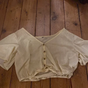 Croppad blus  - Gul croppad blus med knappar och knut i midjan. Skönt och luftigt material som är något genomskinligt. 
