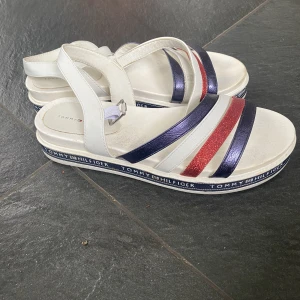 Tommy Hilfiger Sandaler - Tommy Hilfiger sandaler i storlek 40 i vit skinn. Sandalerna är använda, men i fint skick. Skorna är normala i storleken, men passar även storleken 39.
