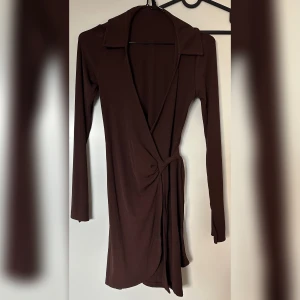 Kort omlottklänning med krage - Storlek S men skulle kunna passa XS också. Brunfärgad. Jag tycker den är mer som en tunika/blus.  Köpt från H&M. ”(StorlekM)  Baksida Längd: 85,7cm.  (Storlek M) Ärm Läng: 64,2cm”