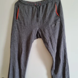 Hugo boss mjukisbyxor  - Grå mjukisbyxor med orangea detaljer. En bakficka. Skada på insida ben, se bild. Finns tillhörande hoodie.