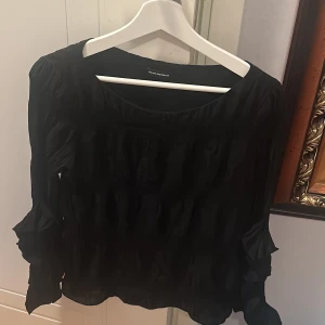 Svart blus  - Säljer denna svarta blus från Club Monaco, har volanger på sidorna och är också lite rynkad i tyget. (Kan skicka närbilder)