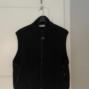 Svart Väst - En svart väst med små neongröna detaljer från weekday. Västen är i bra skick och väldigt sällan använd. Västen är i storlek M.
