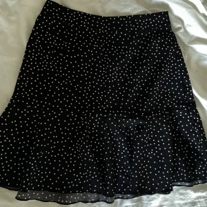 Prickig volangkjol - Prickig kjol med volang längst ner. Hög midja. Bra skick, använd ett fåtal gånger. Har sytt in lite på sidan men det är lätt att sprätta upp