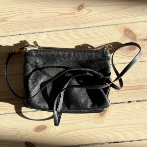 Crossbody läderväska - Axelremsväska i skinn. Har tre delar som kan fästas med knappar. Den e gullig men har tröttnat lite på den då jah använt den mkt!