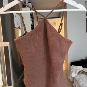 Brun topp med korsad halsringning - Brun topp med korsad halsringning, även justerbara band. Använd några gånger men fortfarande i bra skick. 