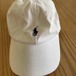 Ralph Lauren keps - Vit Ralph Lauren keps med blått märke som knappt använts. Köparen står för frakten.