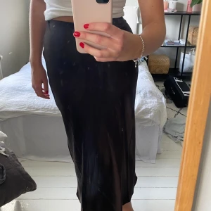 Lång kjol  - Jättefin lång kjol från Lindex i satin, i en mörkbrun färg. Knäpps med en diskret dragkedja i sidan! Varan är i nyskick utan defekter då jag inte använt den mer än en gång. 