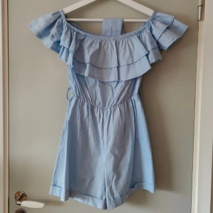 Jumpsuit  - Off shoulder jumpsuit med volang upptill och band i midjan i fin ljusblå färg. Finns en liten fläck (se bild) som säkert går bort vid extra tvätt 