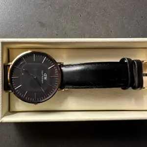 Klocka från Daniel Wellington med svart läderband och roseguld. Uret är i den större modellen. Behöver byta batteri. Har några små repor på glaset som knappt syns. 