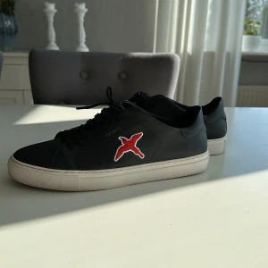 Axel arigato skor - Axel arigato skin skor med röd fågel, köpte de för ett tag sedan men har växt ifrån dom. Storlek 43. Box finns med.
