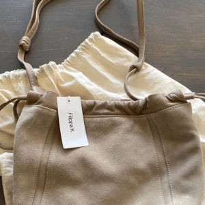 Filippa K - Gråbeige axelremsväska i mocka och skinn från Filippa K. Stängning med magnetlås och läderrem. Storlek: 23*19*14cm. Oanvänd.  Dustbag medföljer.   1000kr 
