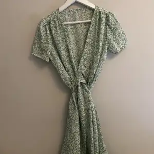 Grön blommig klänning med knytning baktill. Modellen går strax under knäna
