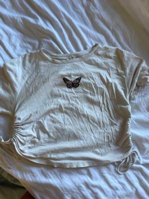 Supersöt och mjuk t-shirt från Urban outfitters med justerbara ihopdragningar på sidorna och en broderad fjäril i mitten av tröjan. Storlek M men skulle säga att den egentligen är xs-s