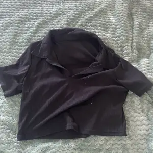 En svart kort T-shirt med krage, aldrig använd. (Det gröna är från kameran)