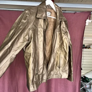 Guldfärgad läderjacka - Inte skrynklig egentligen, men har legat i en påse för länge. Skriv till mig för mer bilder på eller liknande. Jackan är unik, och i helt nyskick. 