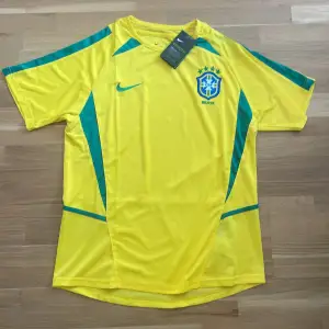 Retro Brasilien Fotbollströja. Tröjan har inget namn på ryggen. Om du vill ha en helt oanvänd Brasilien tröja så är det här perfekt för dig, ja köpte tröjan Som då är storlek L! Men tyvärr så passa den ej.  Pris: 300kr OBS! Pris kan diskuteras!